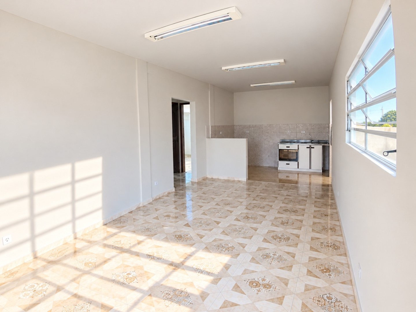 Sala ampla vazia com cozinha iluminada.png